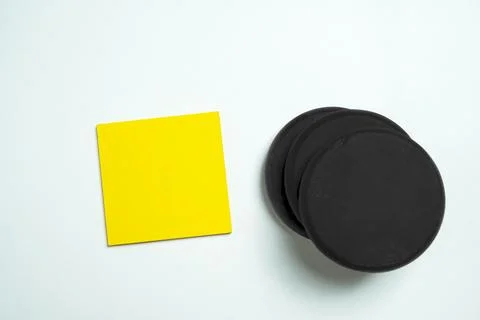 A bright yellow square sticky note placed next to a stack of black round ma.. Stockfoto's