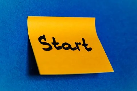 Bright yellow sticky note with handwritten word Start on blue felt background, n Stock Photos