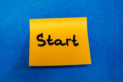 Bright yellow sticky note with handwritten word Start on blue felt background, n Stock Photos
