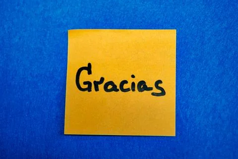 Bright yellow sticky note with handwritten word Gracias on blue felt background, Stock Photos