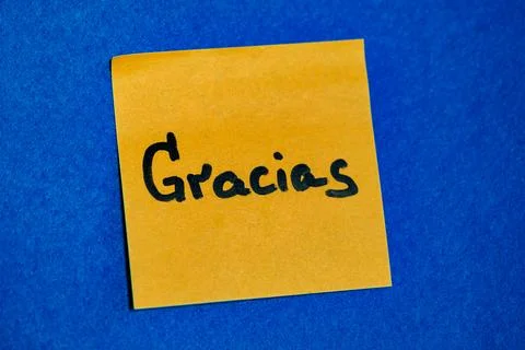 Bright yellow sticky note with handwritten word Gracias on blue felt background, Stock Photos