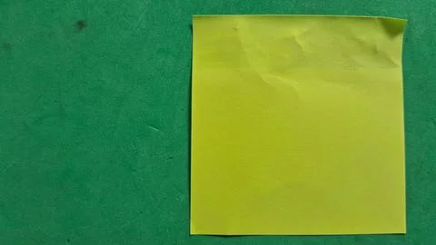 Bright yellow sticky note placed on a textured green background surface Stock Photos