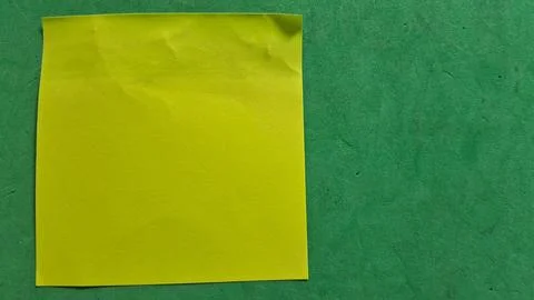 Bright yellow sticky note placed on a textured dark green surface Stock Photos