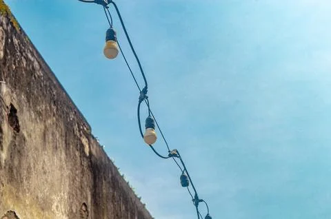 Bright yellow string lights strung across a clear blue sky, with a weathere.. Stock Photos