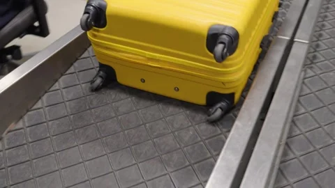 Bright yellow suitcase awaiting its owner at the bustling airport terminal Stock Footage 312050121