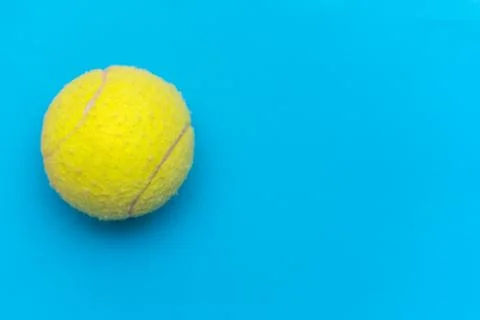 Bright yellow tennis ball on a solid aqua blue flat lay background symbolizin Stock Photos