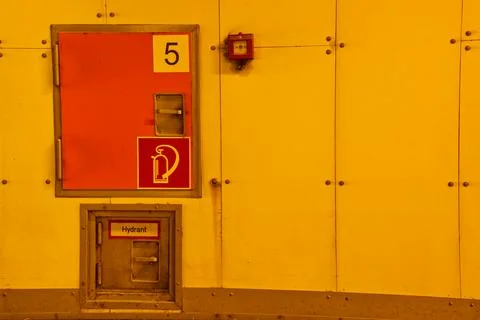 A bright yellow wall featuring a fire hydrant access door and a fire alarm... Stock Photos