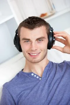 Bright young man listening to music sitting on the couch in the living-room Stock Photos