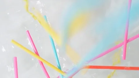 Brightly colored Bent plastic single use straws dropping into water Stock Footage 93994283