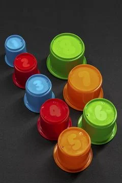 Brightly colored cups with numbers sit on dark fabric Stock Photos