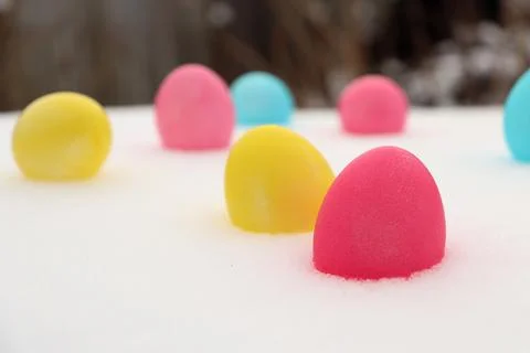 Brightly colored eggs are placed in snow during spring celebration in a backyard 스톡 사진