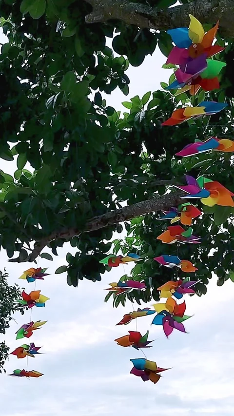 Brightly colored pinwheels spin in the wind, decorating a tree in a park in Stock-Footage 333326756