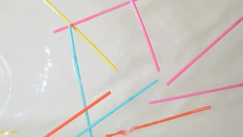 Brightly colored plastic single use straws dropping into water Stock Footage 93993926