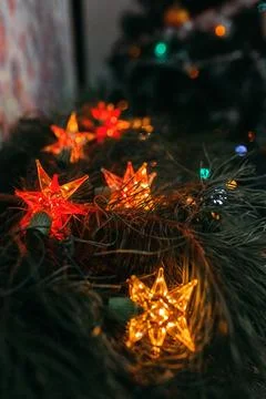 Brightly colored star-shaped lights illuminate a lush green garland, creating Stock Photos