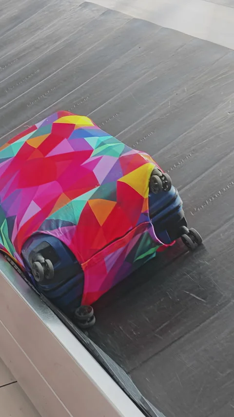 Brightly colored suitcase with a geometric pattern cover moving along a baggage Stock Footage 346185917