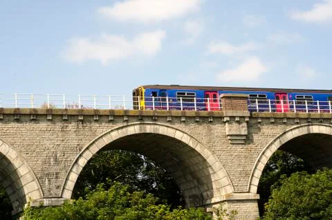 A brightly coloured train  going over old stone bridge Stock Photos