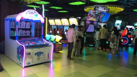 Brightly lit arcade hall featuring electronic game machines and players engaged Stock Footage 331460445