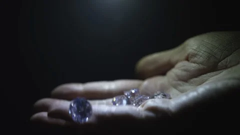 A brightly lit hand opens up and a diamond or gemstones falls away in the light Stock-Footage 117798834