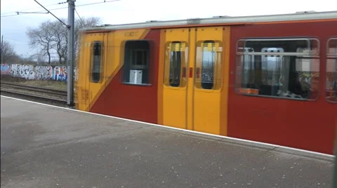 Brightly painted red and yellow electric train leaves station platform Stock Footage 1099382