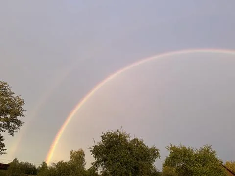 Brilliant double rainbow arching over green trees in rural landscape Foto stock