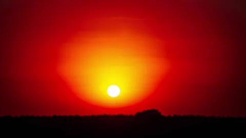 Brilliant sunset with glowing red orb of sun over dark horizon Stock Footage 289374049