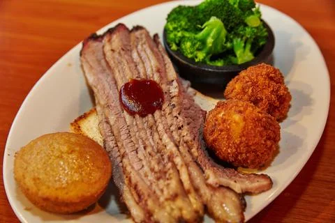 Brisket slices with a side of corn muffin hush puppies and broccoli on a white Stock-Fotos