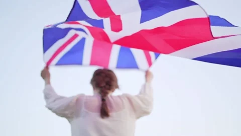 Britain's flag beautifully develops in the hands behind a woman in a slow motion Stock Footage 143157603