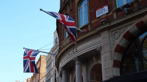 British flags fly in the wind, next to Leicester Square street sign Stock Footage 96271384