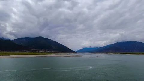 Broad green river below dark mountains and textured gray clouds in Tibet Stock Footage 345884495