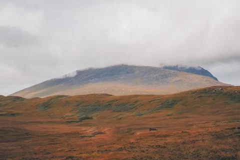 Broad mountain with cloud on its summit beyond orange and green moorland Stock Photos
