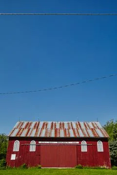 Broad side of a white and red barn with trees, blue sky, and power lines in the 스톡 사진
