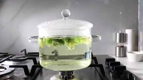 Broccoli boiling in a borosilicate glass pot on a modern gas stove in a bright Stock Footage 345426414