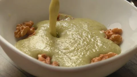 Broccoli soup is poured onto pieces of walnut spilling over the plate Stock Footage 278470544