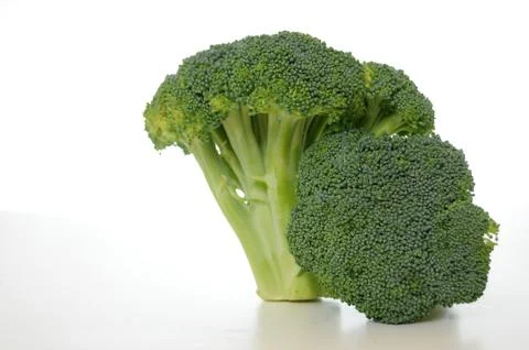 Broccoli vegetable standing on a white shiny table isolated on white backgrou Stock Photos