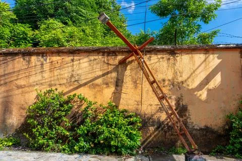 A broken and rusty orange lamp post leaning against a yellow wall Foto stock