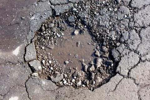 Broken asphalt road with deep pothole filled with water and gravel Stock Photos