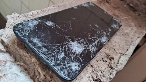 Broken black smartphone screen resting on a rough stone surface Stock Photos