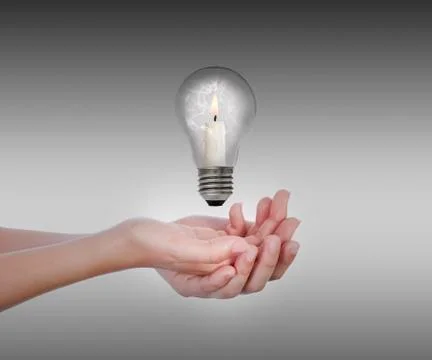 Broken bulb with candle inside levitates on hands Stock Photos