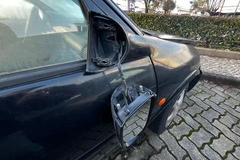 Broken car side mirror hanging from black vehicle door with exposed wires after Stock Photos
