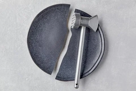 Broken ceramic plate and a kitchen hammer on a light concrete table Stock Photos