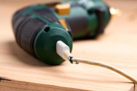 Broken charging wire with torn outer insulation plugged into a cordless screw Stock Photos