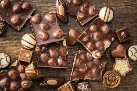 Broken chocolate bars with nuts and pralines on wooden table. Stock Photos