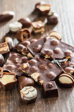 Broken chocolate bars with nuts and pralines on wooden table. Stock Photos