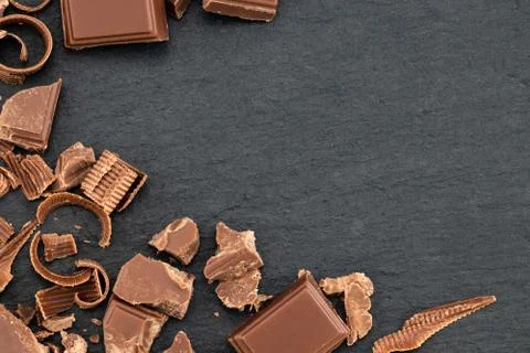 Broken chocolate pieces and chocolate shavings on a dark background. Top view Stock Photos