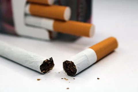 Broken cigarette close up. A pack of cigarettes is out of focus in the Stock Photos