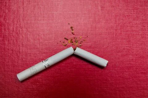 Broken cigarette on a red background. Stock Photos