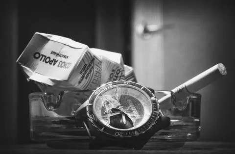 A broken clock on the background of a crumpled pack of cigarettes. Stock Photos