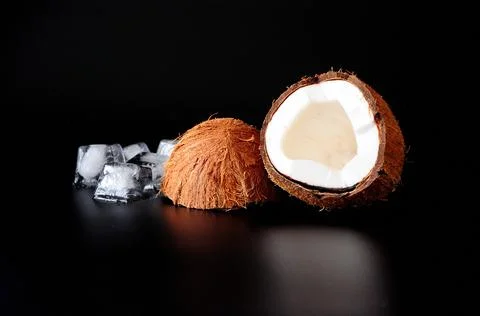 Broken coconut with melted ice cubes on a black background. 库存照片
