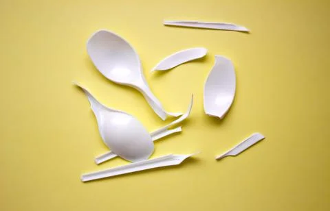 Broken disposable plastic white spoons. Broken plastic on a yellow background Stock Photos