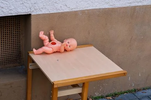 Broken doll abandoned on a small table outside a building in daylight Stock-Fotos